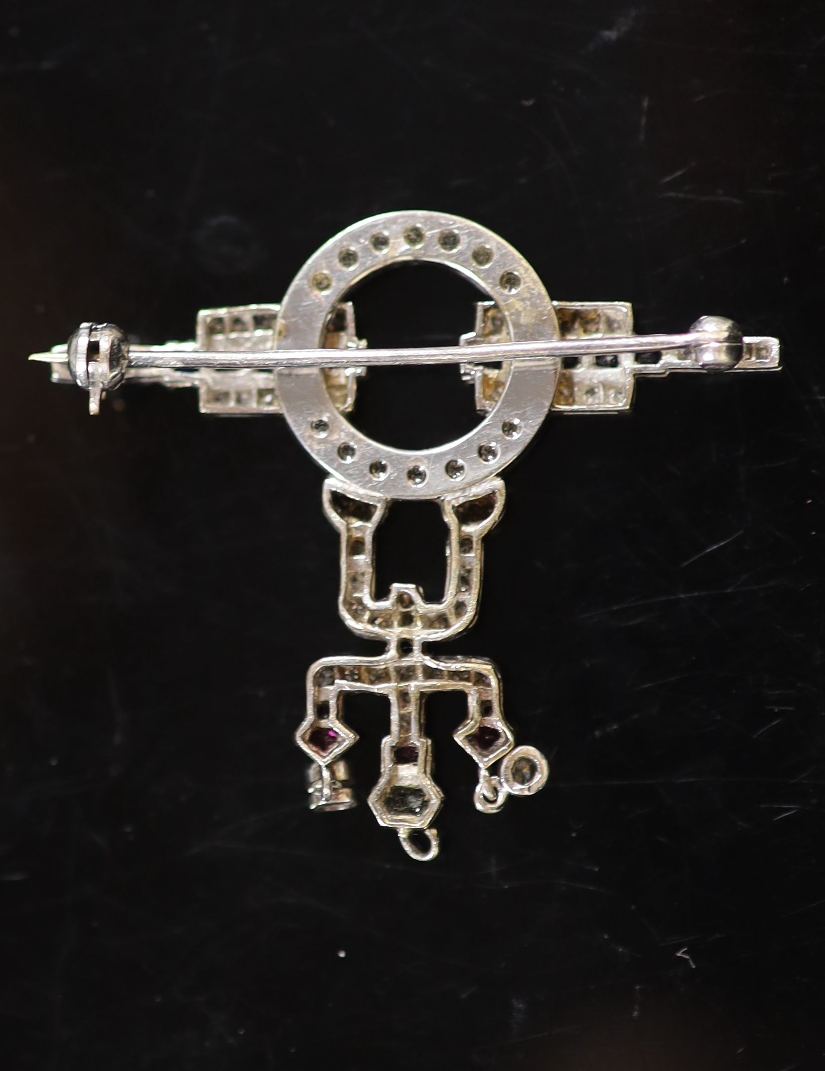 An Art Deco white gold, black enamel, ruby, sapphire and diamond set drop brooch